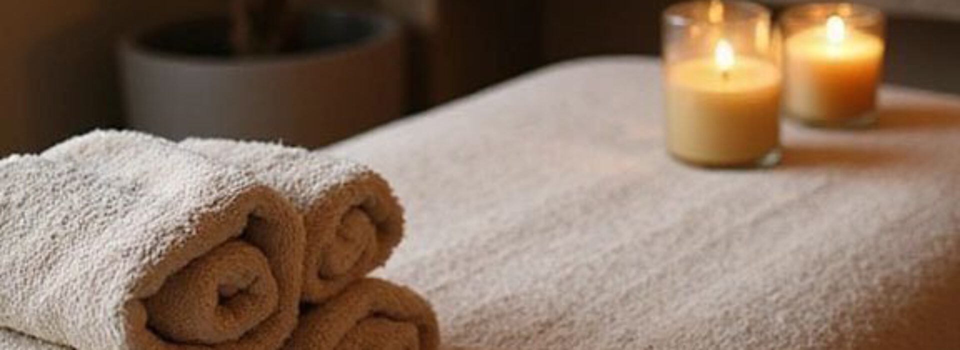 Warm kaarslicht en opgerolde handdoeken bij een massagetafel